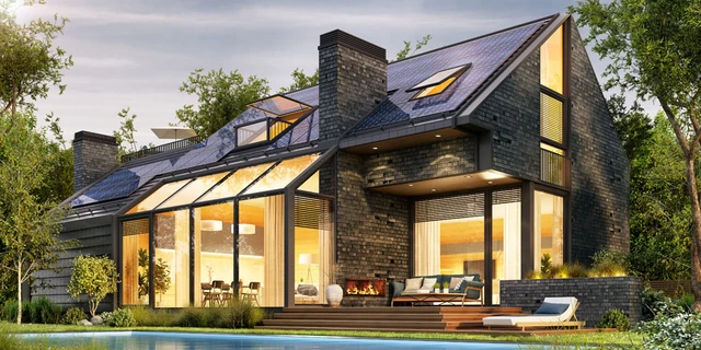 Ein Einfamilienhaus mit Satteldach. Das Satteldach ist mit modernen PV-Modulen ausgelegt. Im Haus brennt Licht.