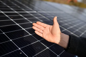 Hilfeanbietende Hand vor einer Fläche mit installierten Solarmodulen, die für erneuerbare Energieerzeugung genutzt werden.