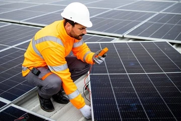 Ein Monteur installiert Solarmodule auf einem Dach und überprüft sie mit einem Messgerät.