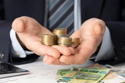 Eine Person sitzt am Schreibtisch mit Euromünzen und 20-Euro-, 50-Euro- und 100-Euro-Scheinen.