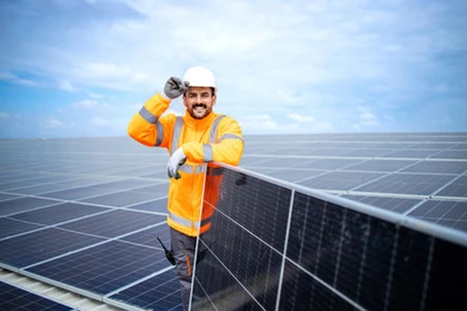 Facharbeiter für PV-Montage auf dem Dach, der lächelnd in die Kamera blickt und ein Solarmodul festhält.